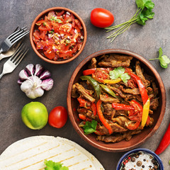 Traditional mexican dish fajitas meat with vegetables and salsa sauce on a dark rustic background. Flat lay, overhead.