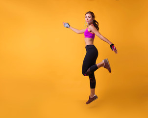 Fototapeta na wymiar Inspired woman training in headphones. Slim caucasian girl doing excersizes.Woman in sportswear running over yellowbackground. Full length shot of healthy young caucasian woman sprinting. Copy space.