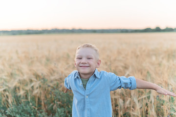 Handsome blond boy with blue eyes is running in a wheat field