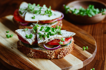 Sandwiches with turkey meat and fresh vegetables served with microgreens on a wooden plate. The concept of healthy and diet eating.