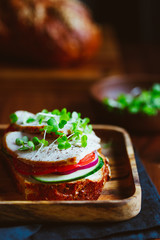 Sandwich with turkey breast and fresh vegetables served with microgreens on a wooden plate. The concept of healthy and diet eating.