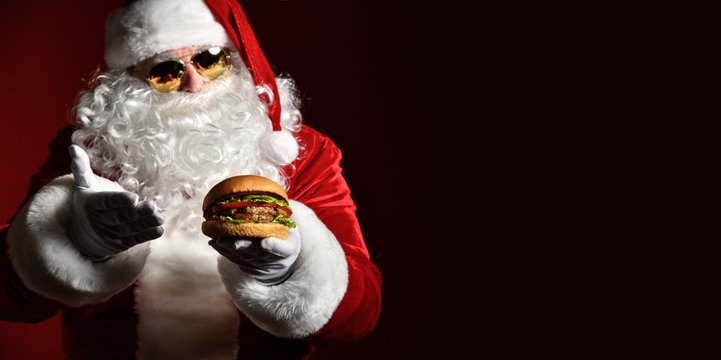 Happy Santa Claus in stylish sunglasses offer tasty burger sandwich hamburger in hand. New year