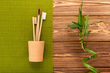 Bamboo toothbrushes in hand made clay glass bamboo plant with green towel on wooden background.Flat lay.Biodegradable natural bamboo toothbrush.Eco friendly,Zero waste,Dental care Plastic free concept