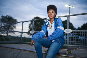 Attractive young african american woman skaterboarder sittting o