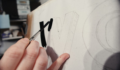 An artists hand with a paint brush painting retro letters and typography graphics. Artists hand...