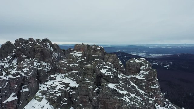 Aerial view; drone flies over rocky peaks of mountain ridge Otkliknoy Greben'; dangerous climbing route for tourists in winter; snow-covered stone and boulders; panorama of Ural mountains in foggy day