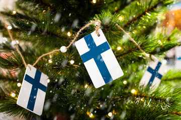 Flags of Finland on a Christmas tree with garland lights in focus. Background and snowfall blurred.