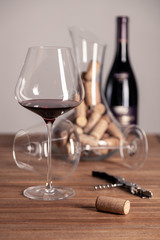 Crystal red wine glass, bottle, corkscrew, opener, sommelier knife, transparent decanter, corks on wooden table. Closeup, vertical, selective focus, side view. Concept degustation in winery cellar
