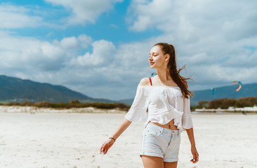 a girl with a high ponytail of hair goes forward along the beach, looks over her shoulder, covering...
