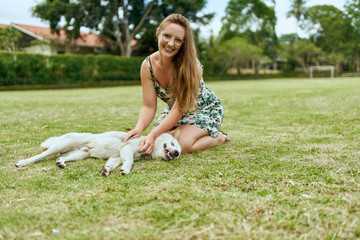Young, beautiful blonde girl playing outdoors with friendly pupp
