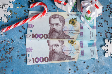 Ukrainian 1000 hryvnia on a blue background with stars, gifts, snowflakes, sweets and Christmas tree. The concept of buying Christmas and New Year gifts in Ukraine