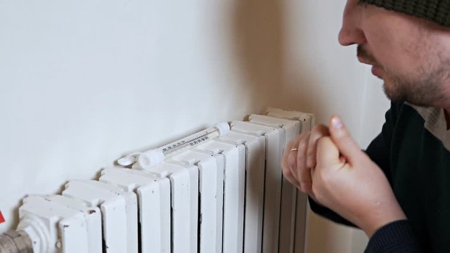 Man checking the temperature of the heating battery. Cold winter, cold in the house, apartment. A man warms himself near a heating battery