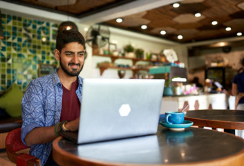 Handsome millennial indian man working in trendy coworking space - obrazy, fototapety, plakaty