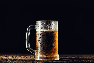 Beer. Cold Craft light Beer in a glass with water drops on the wooden table over the black background.