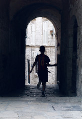 Fototapeta na wymiar an atmospheric alleyway with a silhouette of a boy running through having fun in an ancient city in europe. young generation in an old environment. youth playing in an urban setting.