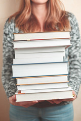 A stack of books is held by a woman. Books are in focus. The background is blurry.