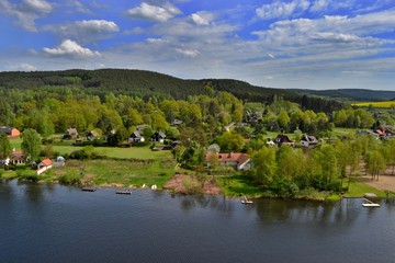 Beautiful village in woods along the river Vltava. Lush green trees, yellow fields, blue sky, white clouds. Roviště - Kamýk nad Vltavou, Czech Republic.  - obrazy, fototapety, plakaty