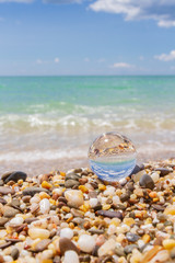 Obraz na płótnie Canvas Glass round ball on the beach reflects the sea in summer