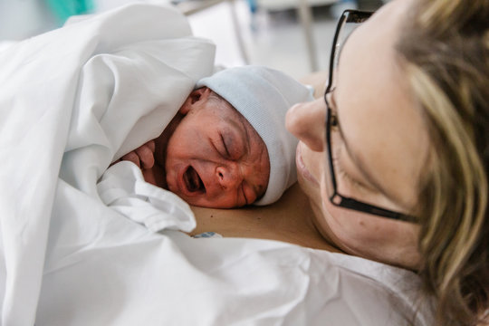 mujer madre con bebé hijo recién nacido (neonato) llorando y haciendo el piel con piel  en la cama del hospital, clínica.
