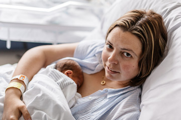 mujer madre con bebé hijo recién nacido (neonato) dormido haciendo el piel con piel en la cama del hospital, clínica. - obrazy, fototapety, plakaty
