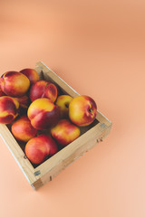 A wooden box full of nectarines, on a peachy color background
