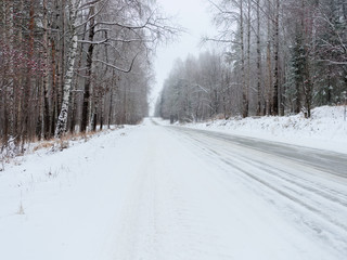 Rural road in the forest covered with snow. Travel on a snowy road on a winter day through the forest