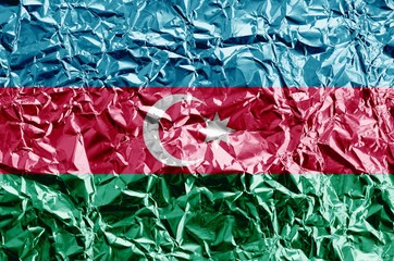 Azerbaijan flag depicted in paint colors on shiny crumpled aluminium foil closeup. Textured banner on rough background