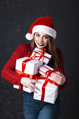 Lovely girl with make-up in a burgundy sweater and santa claus hat. Posing on a dark background holds gifts on a Christmas tree, the concept of Christmas and New Year
