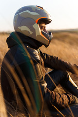 Profile portrait of a sportsman Biker standing on yellow fields and looking at sunset, in sunny day. Vertical view. Freedom, sport, drive, strength concept.