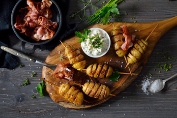 Gebackene Kartoffelspiralen am Spieß mit frischem Kräuterquark und gebratenem Speck serviert –...