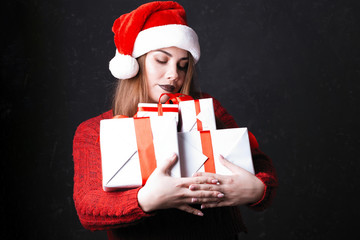 Lovely girl with make-up in a burgundy sweater and santa claus hat. Posing on a dark background holds gifts on a Christmas tree, the concept of Christmas and New Year