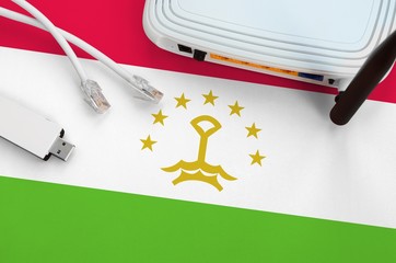 Tajikistan flag depicted on table with internet rj45 cable, wireless usb wifi adapter and router....