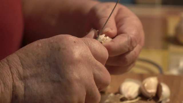 Elderly woman peeling garlic in the kitchen.