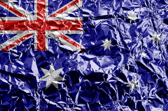 Australia flag depicted in paint colors on shiny crumpled aluminium foil closeup. Textured banner on rough background
