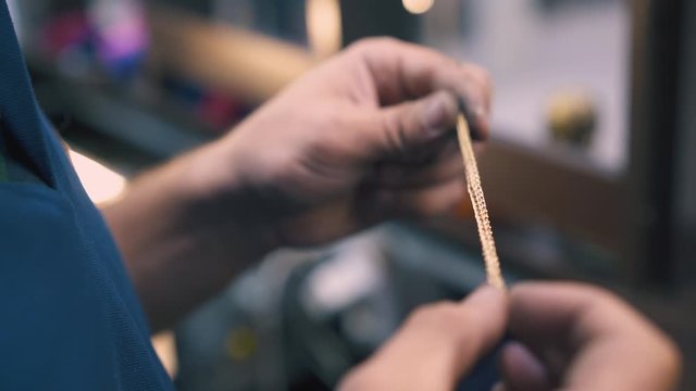 CU: skilled jeweler holds new gold bracelet in hands examining on blurred background in light workshop close view