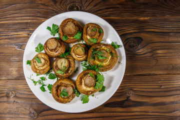 Baked mushrooms in plate on wooden table. Top view