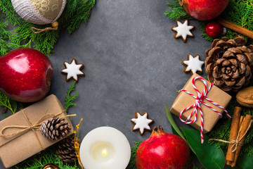 Festive botanical Christmas composition from natural materials green cypress red apples gift boxes cookies, pomegranates pine cones burning candle on dark background