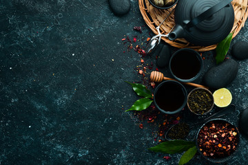 Set of black, green, fruit and herbal tea on black stone background. Tea in teapot and cup. Top view. free space for your text.