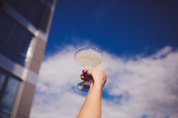 cocktail glass in the hands on sky background. Summer vacation concept