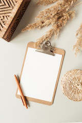 Flat lay minimalist home office desk with blank sheet clipboard with copy space for text, reeds branch, casket on neutral background. Top view work, business, education template.