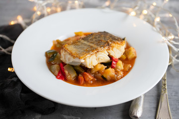 cod fish with vegetables in white plate on ceramic background