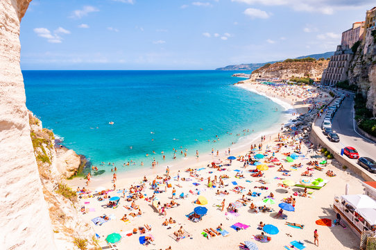 Rotonda beach full of people. Amazing Italian beaches. Sea promenade scenery in Tropea with high cliffs with built on top city buildings and apartments.