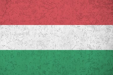 Hungary flag depicted in bright paint colors on old relief plastering wall. Textured banner on...