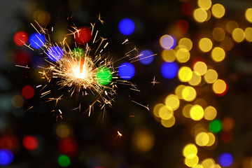 Burning sparkler with flying sparks. Blurred background with colored spots. Concept - New Year, Celebrating Party.
