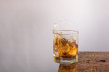 ice falls into a glass standing on the edge with whiskey and splashing on a gray background