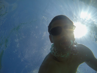 Young caucasian Man with sunglasses swimming underwater and looking at camera