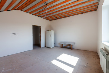 Fototapeta na wymiar Construction site of residential building interior in progress to new house. Empty renovation white room with window and wooden beams for ceiling roof with a few pieces furniture