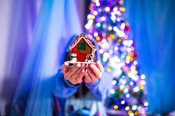 Girl in warm blue dress holds a small Christmas house
