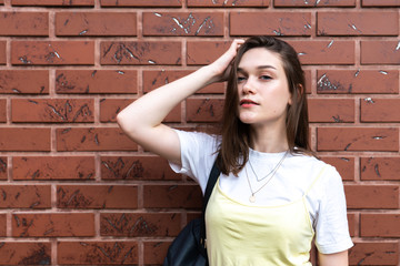Sensual brunette girl with natural makeup holds her hand on her head and looking at the camera isolated over red brick wall