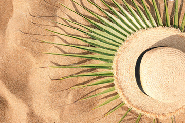 Green leaf of palm tree and straw hat on yellow sand at the beach